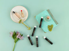 Ein flachgelegtes Set von SanaExpert Collagen Beauty Elixir Flaschen, umgeben von Schönheitsprodukten und einem Notizbuch auf türkisem Hintergrund.