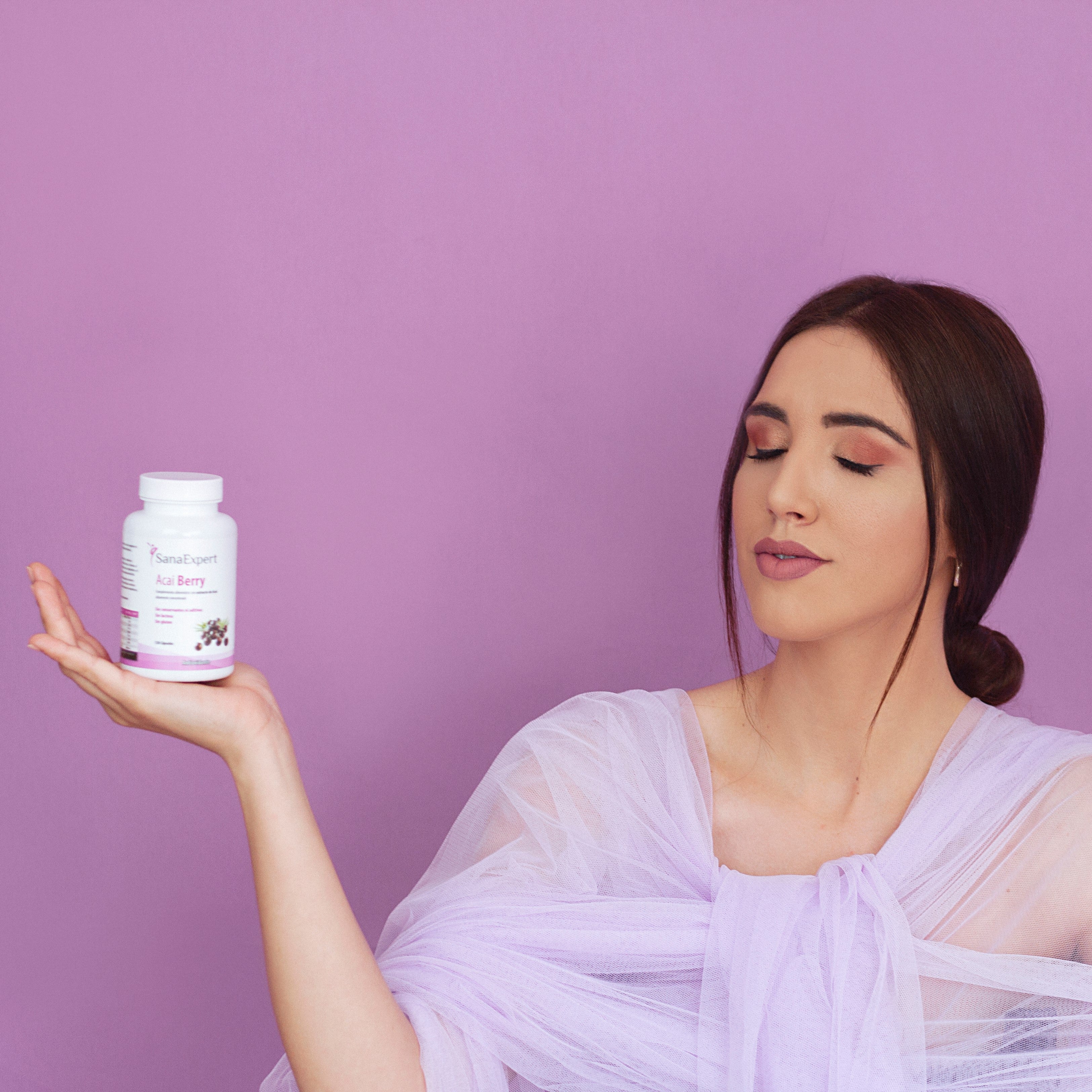 Eine Frau in lila Kleidung balanciert sorgfältig eine Flasche SanaExpert Acai Berry Nahrungsergänzungsmittel auf ihrer Handfläche.
