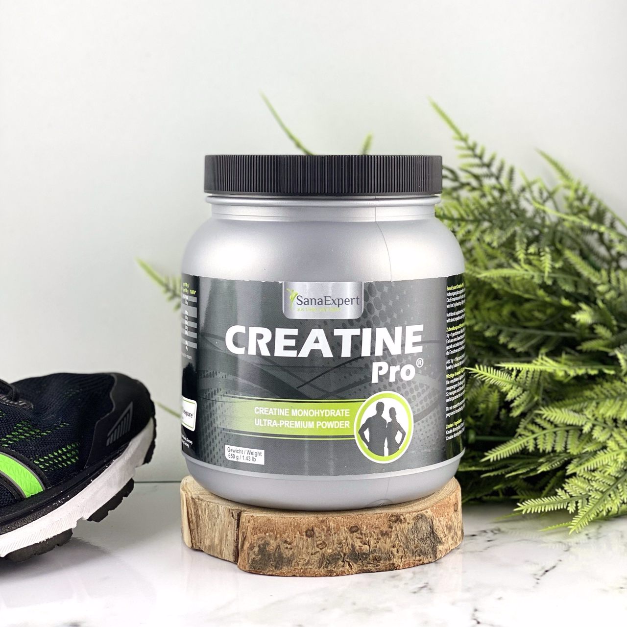 Creatine Pro Dose auf einem Holzstück neben einem Laufschuh und grünen Pflanzen, neutrale Farbgebung.