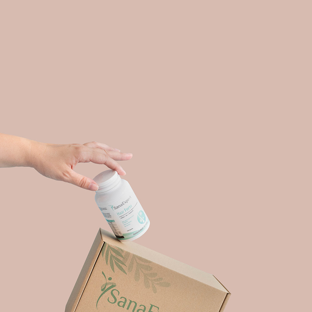 Eine Hand platziert eine Flasche SanaExpert Haar Forte neben einer Pappschachtel auf einer pastellfarbenen Oberfläche.