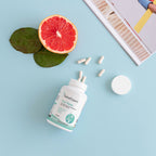 Ein geöffnete Flasche SanaExpert Haar Forte neben einer halbierten Grapefruit und Kapseln, arrangiert auf einem blauen Hintergrund.