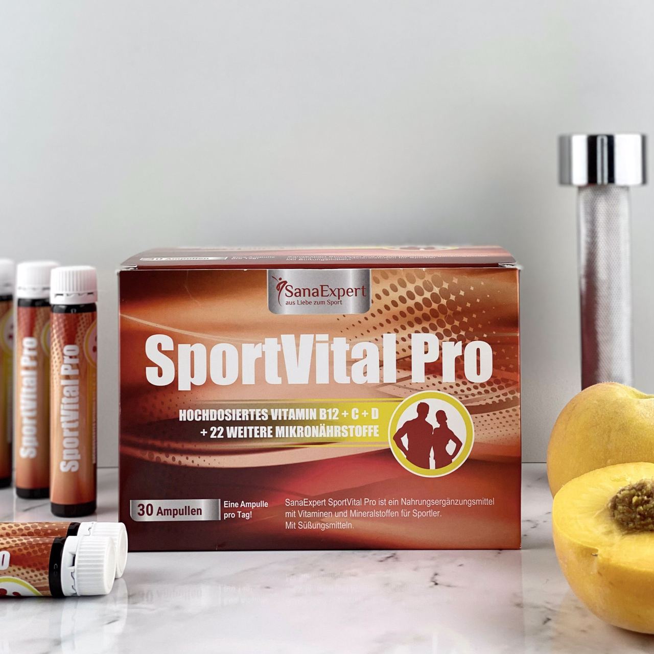 SportVital Pro Packung und Ampullen auf einer marmorierten Oberfläche, neben einer Wasserflasche und einer aufgeschnittenen gelben Frucht.